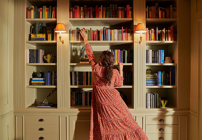 A woman reaches for a book in a library at Gleneagles Townhouse
