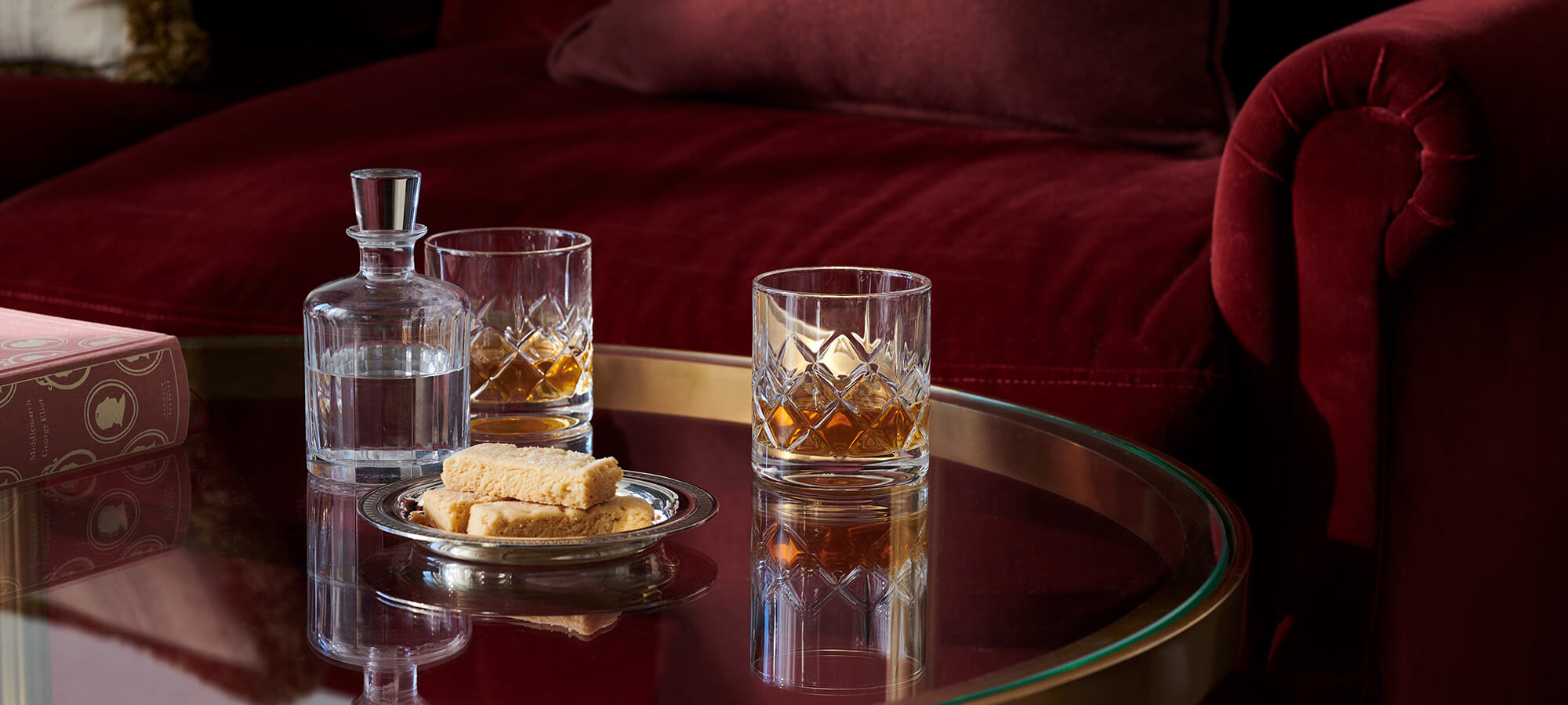 Two crystal glasses of whisky and silver tray of shortbread on a glass table in an Estate Room in Braid House
