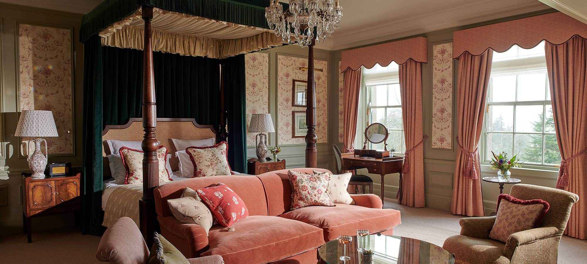 A large four poster bed, red velvet sofa, multiple tables and chairs sit in a the Royal Lochnagar Suite