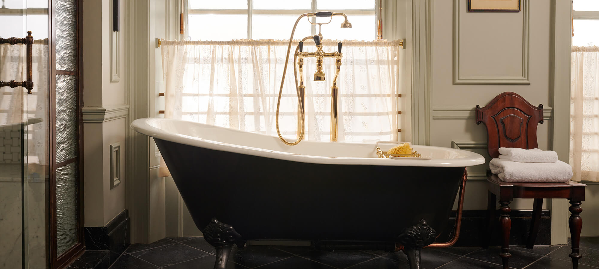 A large green roll top bath with gold taps and shower in the Royal Lochnagar Suite