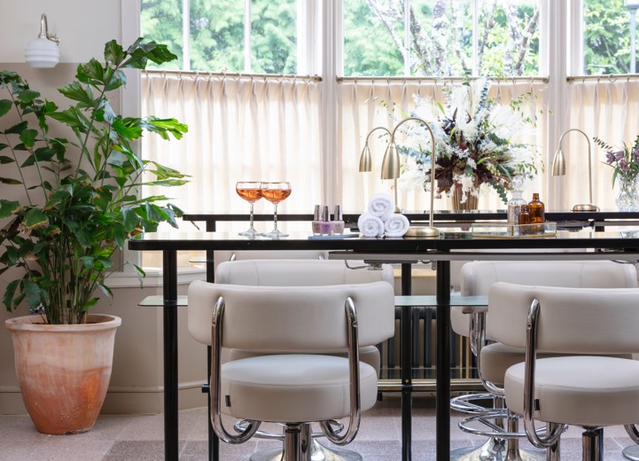 Two glasses of rose champagne sit on top of a manicure bar with white leather chairs and large plants