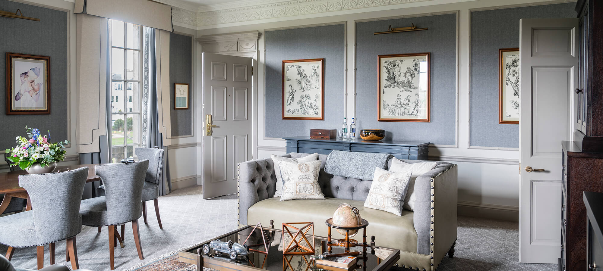 a large blue sitting room with grey leather sofa and grey chairs around a dark wood table in a one bedroom whisky suite