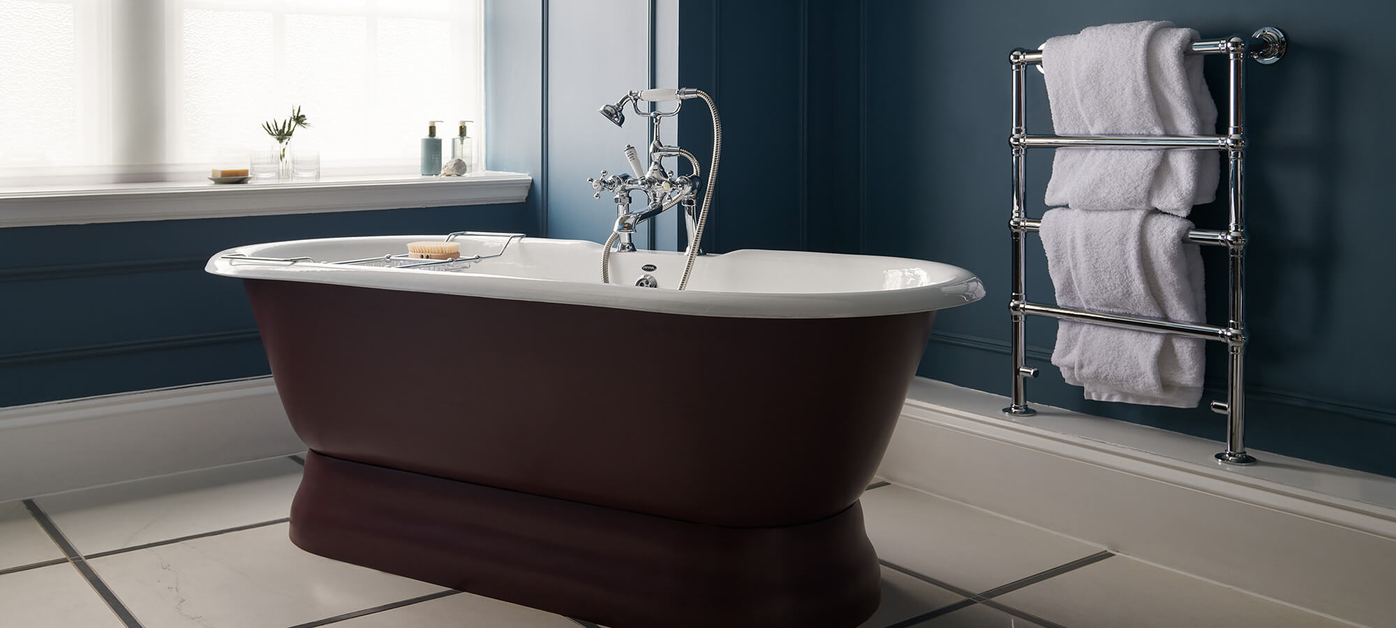 A large plum coloured bfree-standing bathtub in a navy blue bathroom in a Manor room