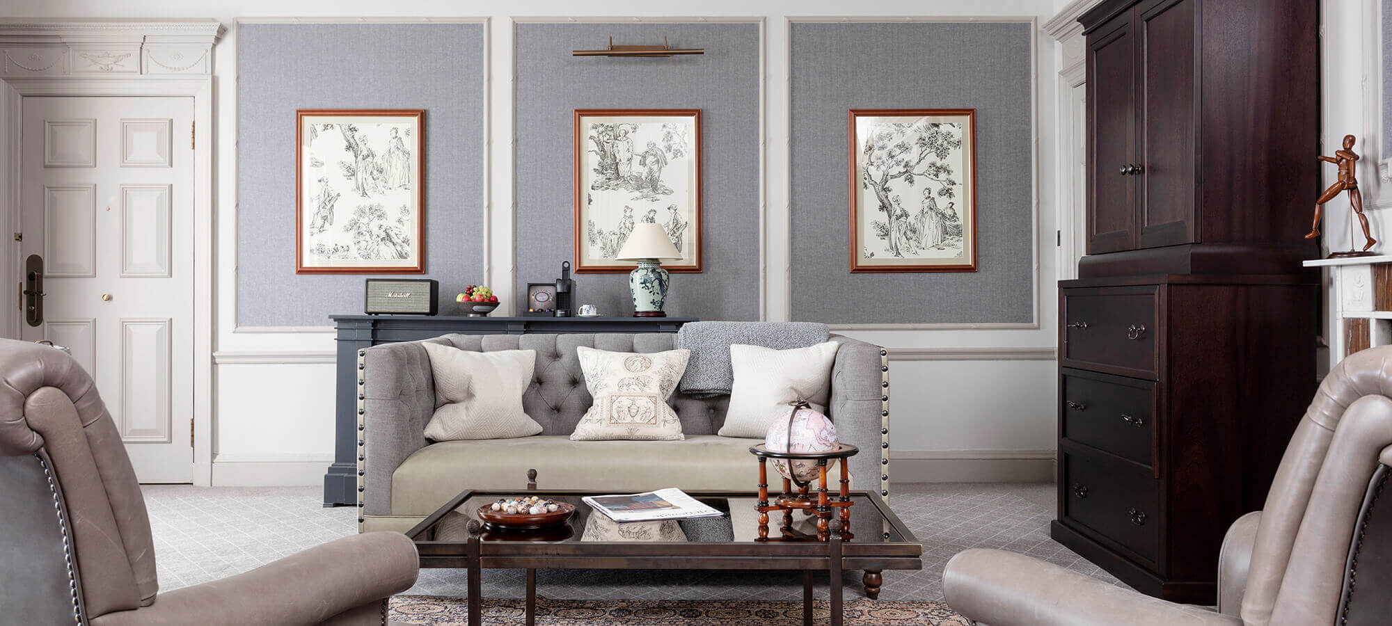 A large grey leather sofa sits at the back of a beautiful suite sitting room with two sitting chairs in the foreground in an estate suite