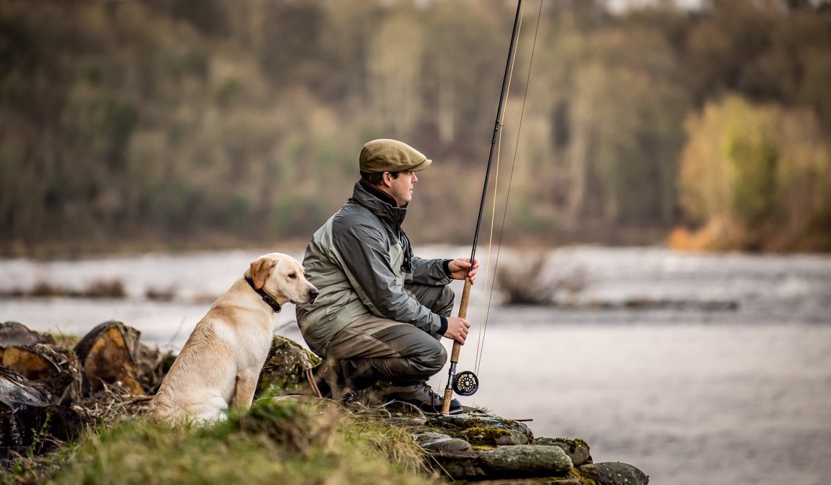 A fisherman and his dog sit next to the river tay