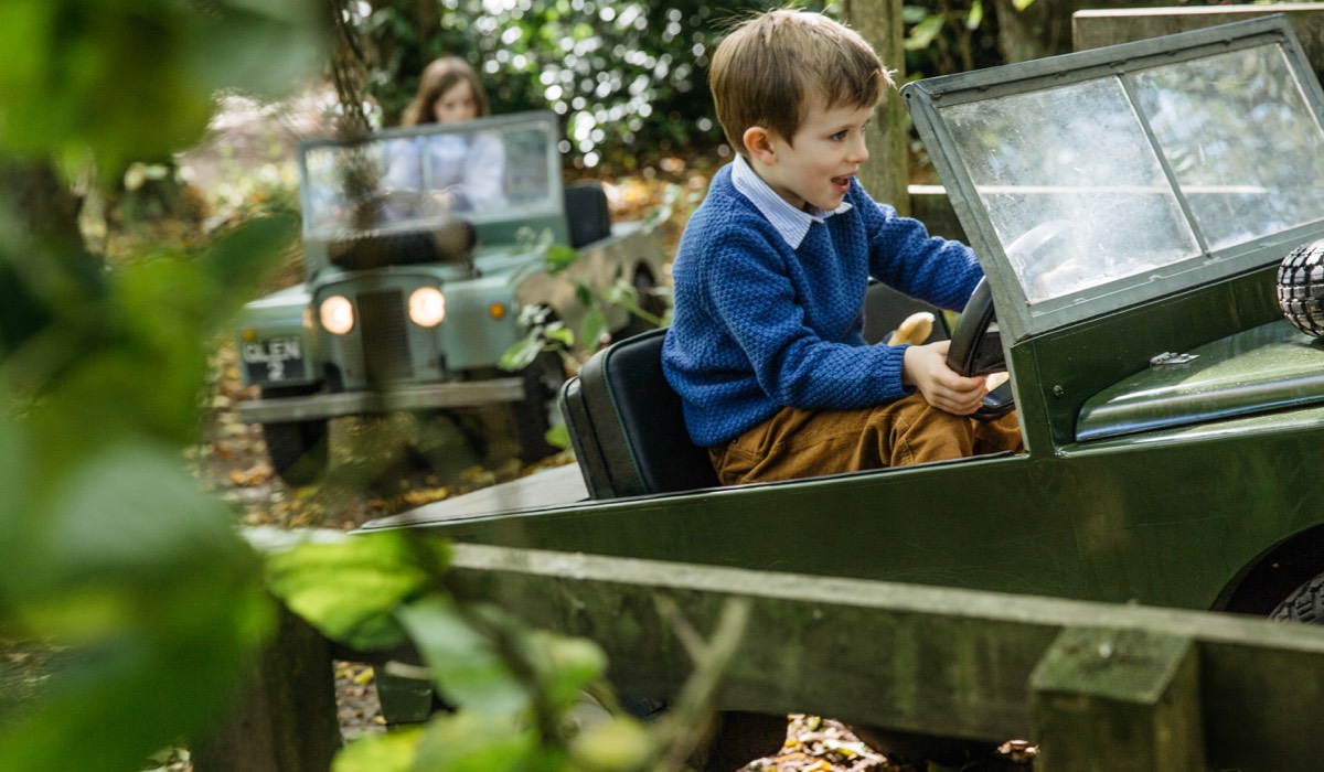 A boy in a blue jumper drives a mini Land Rover replica