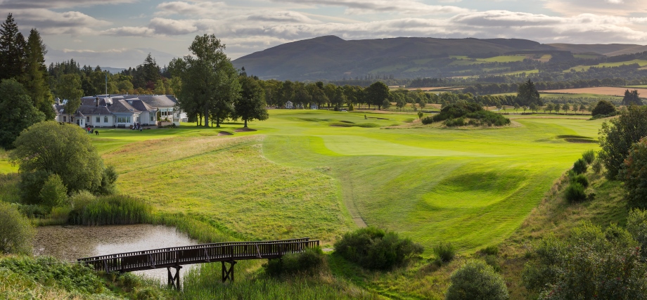 The 18th hole of the queens Course with a river and bridge in the foreground and Ochil Hills in the background.