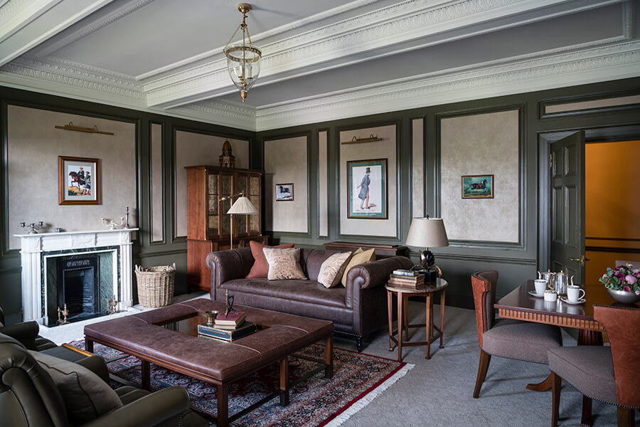 Dark grey leather sofa and ottoman in a dark green painted living room