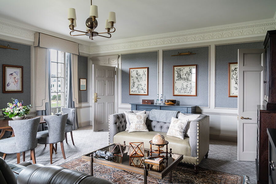 A large, blue sitting room with leather sofas and antiques on the coffee table