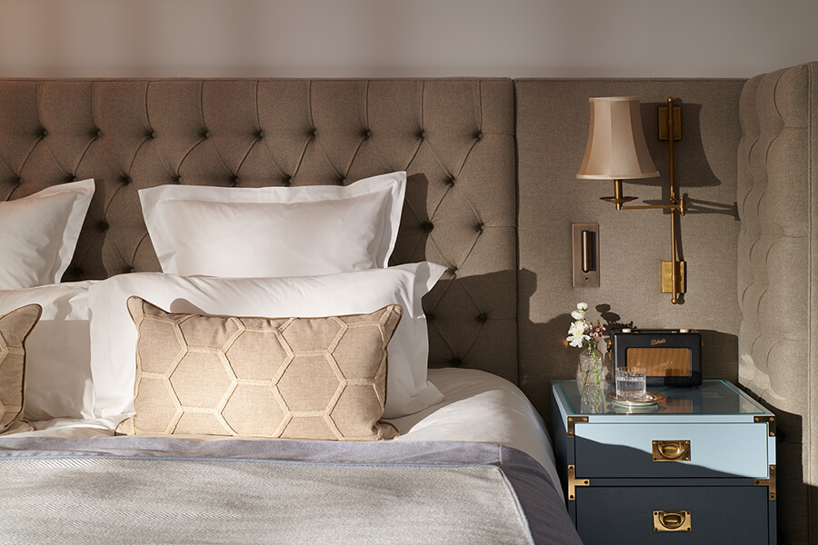 A close up of pillows on a bed and a blue bedside chest of drawers with Roberts radio on top