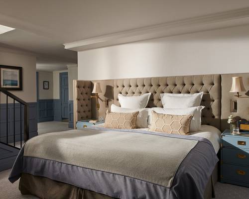 A king sized bed surrounded by a large cushioned headboard and two blue bed side chests of drawers