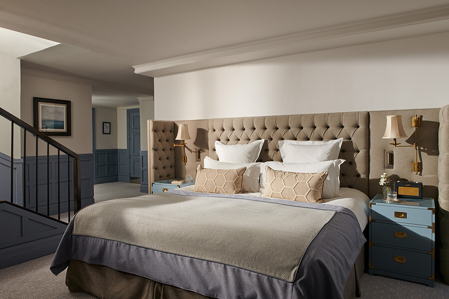 A king sized bed surrounded by a large cushioned headboard and two blue bed side chests of drawers