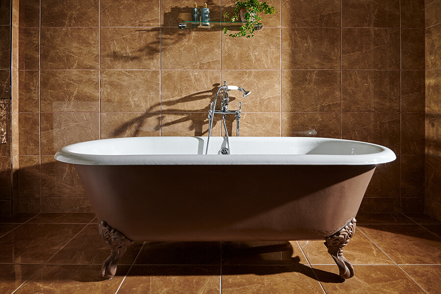 A large rollmop bath sits centrally in a brown marble bathroom