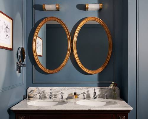 A marble double vanity bathroom sink with double oval mirror and sky blue painted walls in an estate bedroom's bathroom