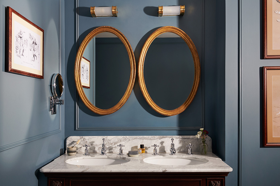 A marble double vanity bathroom sink with double oval mirror and sky blue painted walls in an estate bedroom's bathroom