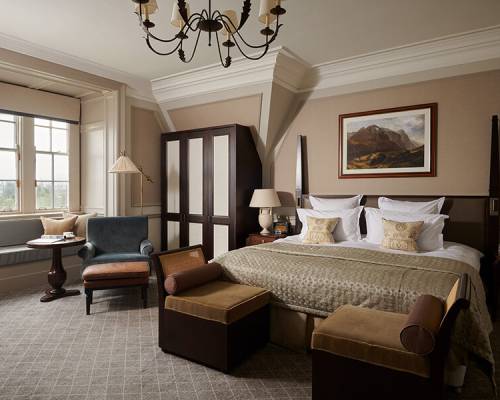 A large manor bedroom with king sized bed and bay window seating