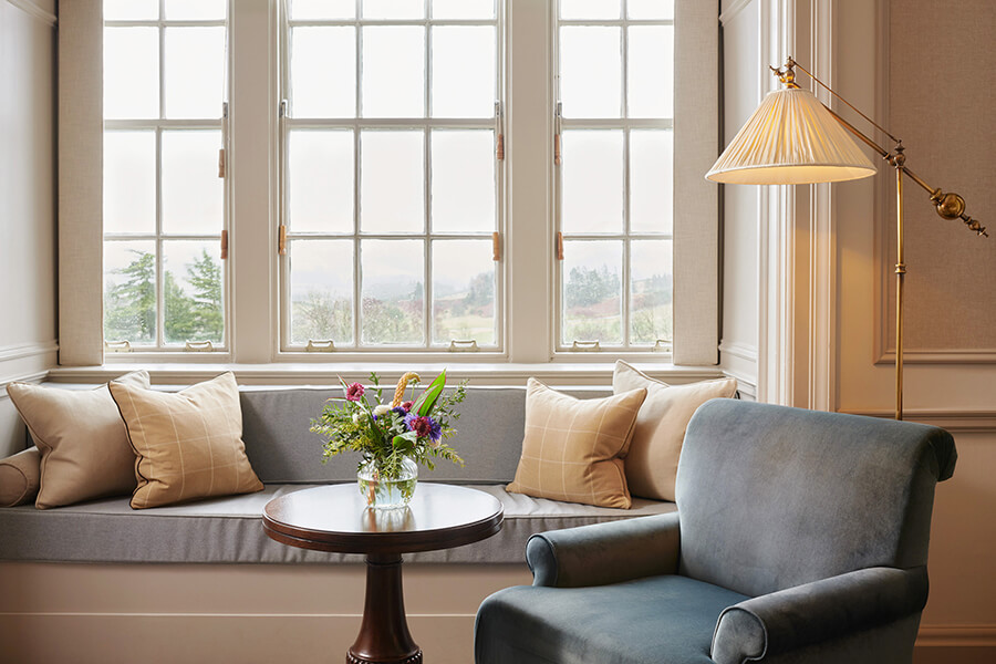 A blue arm chair and reading lamp sit in from of a bay window and bench seat