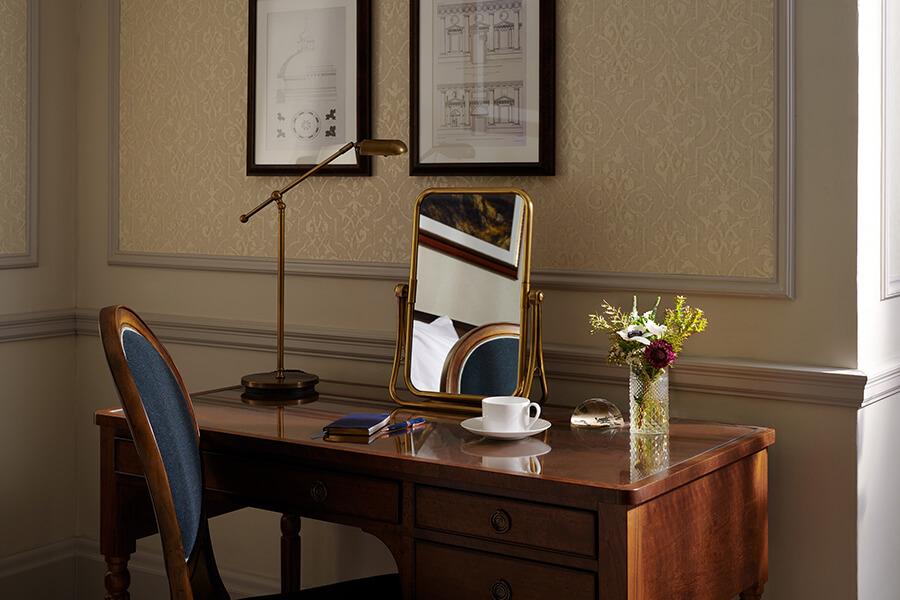 A walnut dressing table with brass mirror, reading lamp and cup and saucer of coffee in a Country bedroom