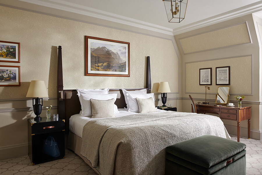 An elegant king sized bed with a painting of a mountain landscape above it sits in the middle of a luxury Country bedroom at Gleneagles