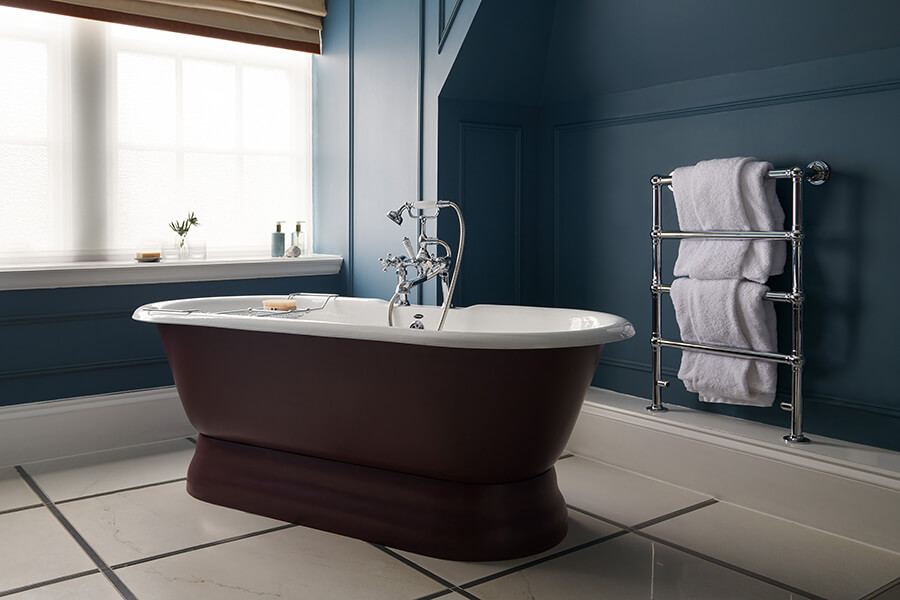 A large purple rolltop bath in the corner of a dark blue bathroom in a Manor Bedroom