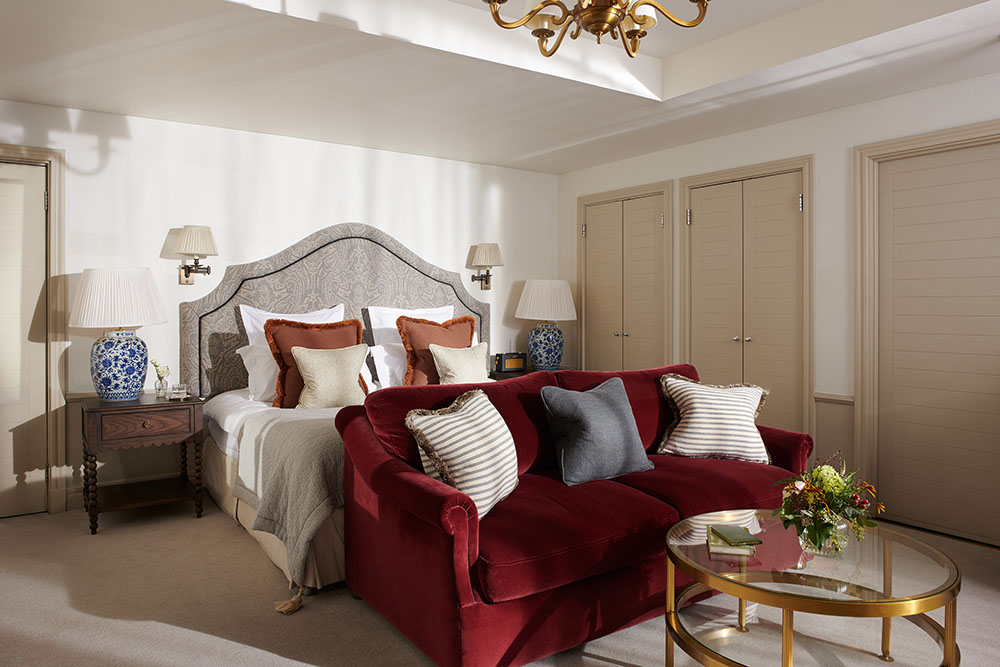 A large red sofa sits at the bottom of a king sized bed in a Braid Estate bedroom with numerous luxury lights, tables and ornaments