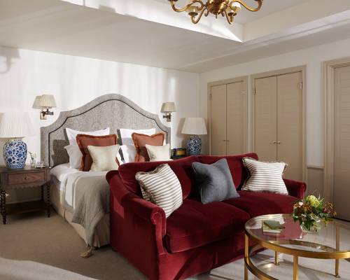 A large red sofa sits at the bottom of a king sized bed in a Braid Estate bedroom with numerous luxury lights, tables and ornaments