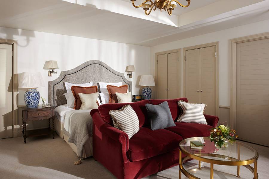 A large red sofa sits at the bottom of a king sized bed in a Braid Estate bedroom with numerous luxury lights, tables and ornaments