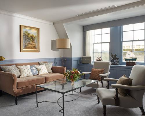 A large blue living room with glass coffee table, pink sofa and two grey armchairs
