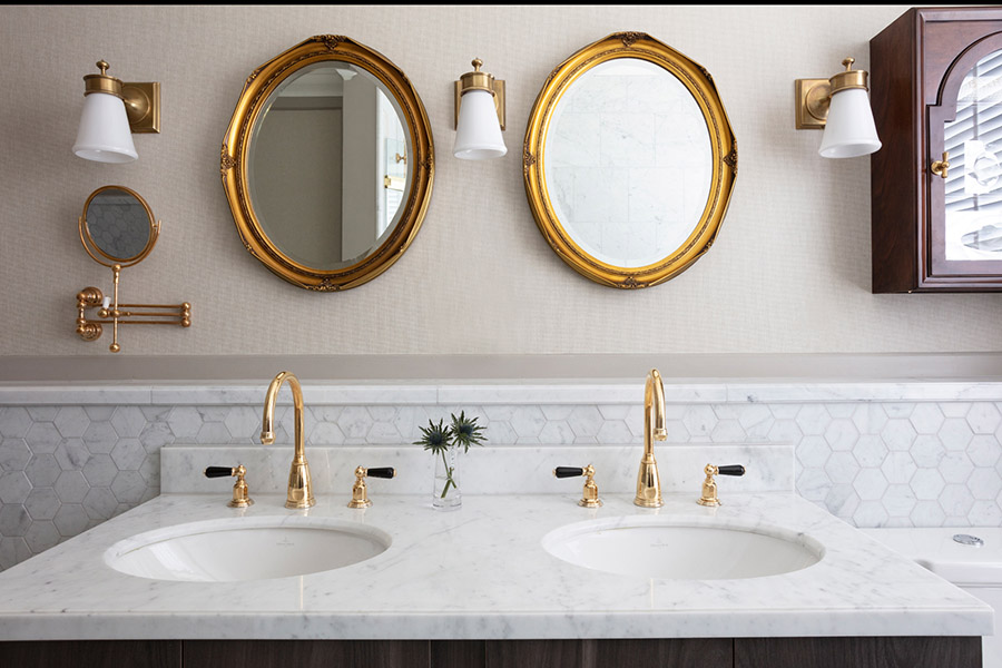 Two large gold oval mirror above a double vanity marble washbasin