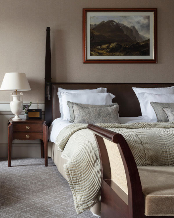 A large luxurious bed with painting above it and side table with large lamp and Roberts radio next to it
