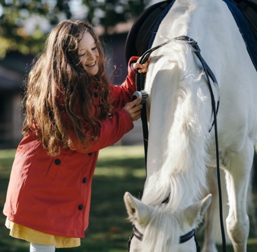 A young girl in a red coat pats a grey pony