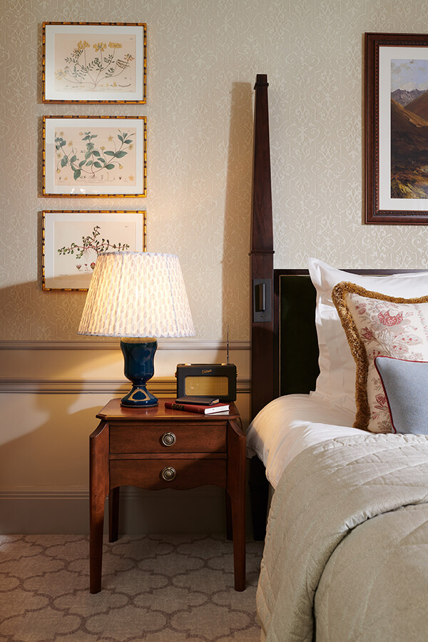 A bedside table with large lamp and Roberts radio sit next to a king size bed in a Country room