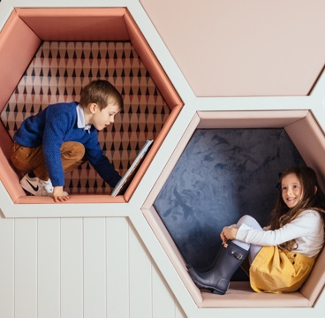 Two smiling children sit in hexagonal cubby holes in the wall in The den at Gleneagles