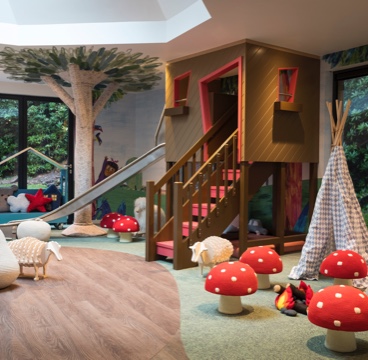 A large treehouse shaped climbing frame in the middle of a kids playroom