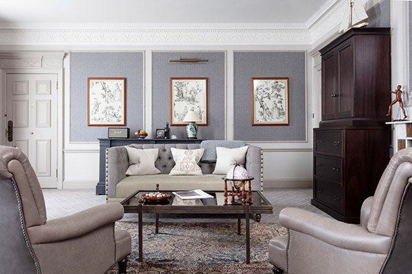 A triptych of images sit on a wall behind a grey leather seating set and glass and mahogany table