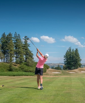 A woman dressed in a pink polo and white cap drives off a tee on a sunny day at Gleneagles