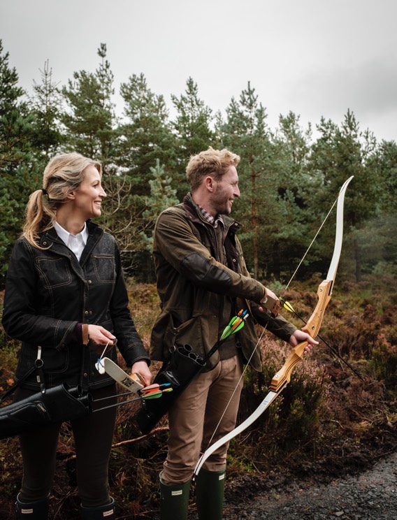A couple with bows shooting arrows in woods at Gleneagles