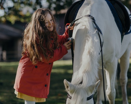 A young girl in a red jacket smiles as she pats and white pony at Gleneagles
