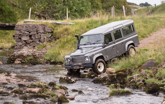 A large land rover defender approaches the entry to a river next to a stone bridge in an off-road driving experience