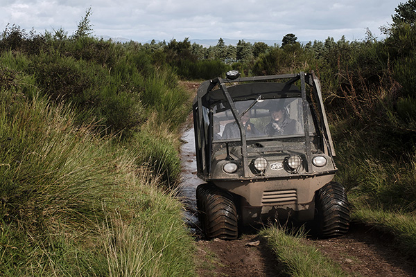 An instructor and guest drive an argocat along a dirt track surrounded by vegetation during an off-road lesson