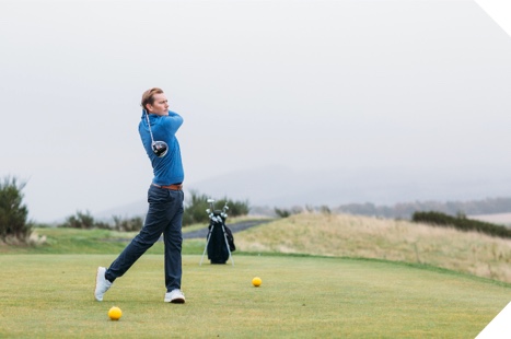 A golfer in a blue top tees off on a misty day at Gleneagles
