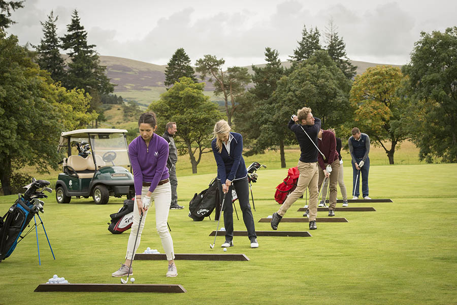 A group of golfers receive tuition on a driving range on a corporate golf day