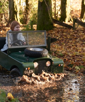A young girl drives a replica land rover defender through a puddle in a junior off-road driving lesson