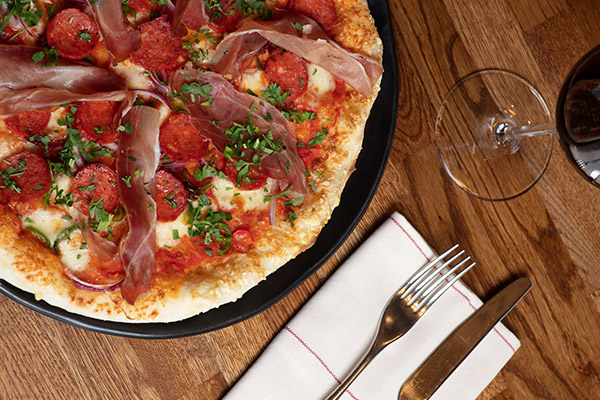 A whole pizza with salami and tomato topping served with a glass of red wine