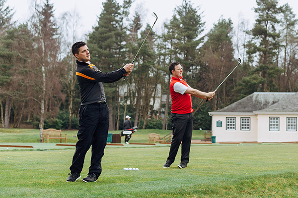 Two golfers hit practise balls on a driving range