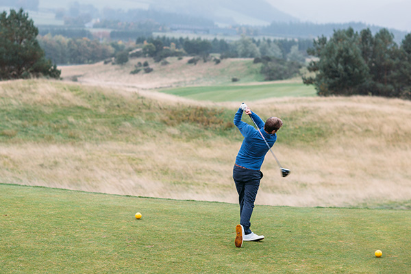 A golfer driving off a tee at Gleneagles on a misty autumnal day