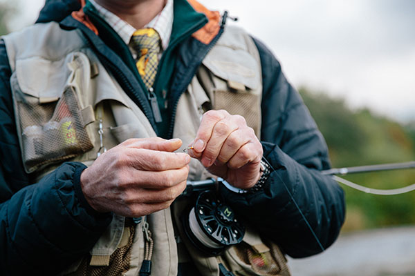 A fisherman tying a fly on the banks of a river