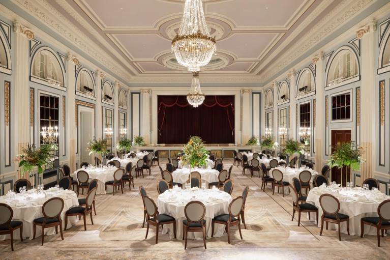 A ballroom with chandeliers set up with round tables for a large dinner