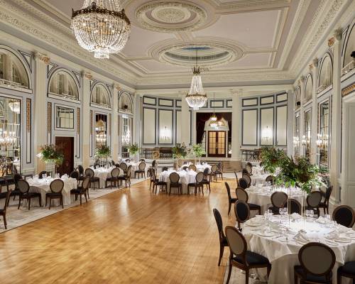 A huge ballroom with wooden floor, round tables, chandeliers and large floral arrangements at Gleneagles