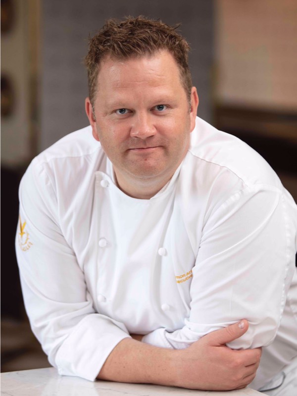 Simon Attridge in chefs whites leans on a marble table